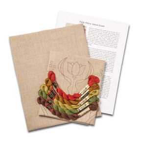 Overhead view of a DIY embroidery kit for a tulip pillow design, showing folded natural linen stamped with a tulip alongside arranged embroidery thread skeins in a variety of colors.