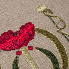  Closeup photo of a linen dark beige table scarf featuring embroidered artwork of a red poppy design.