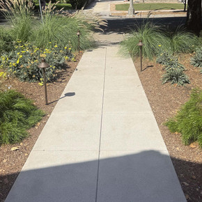  A concrete path leading to the horizon flanked by plants and patinated copper pathway lights with flared roofs. 