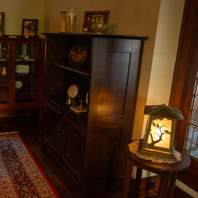  A rustic, Arts & Crafts style lantern with raven artwork on wood furniture filled with odds and ends in a historic home.