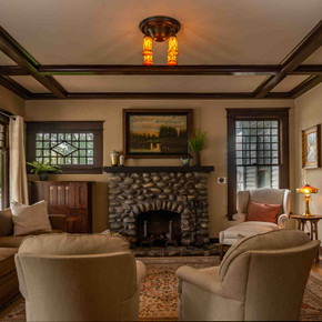  The living room in a transitional historic home restored by Brett Waterman. There is a stone fireplace, neutral furniture and a custom ceiling light fixture with cherry blossom shades.