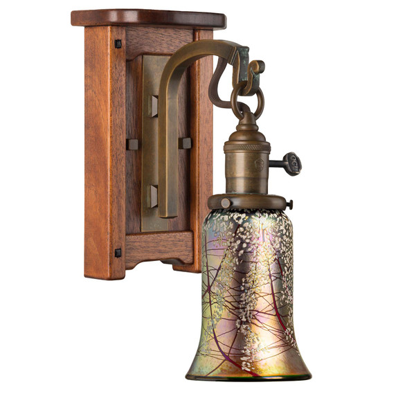  An Arts & Crafts wall sconce light fixture with a wood backplate featuring rounded corners and ebony peg accents. The lantern has a turn key socket, an aged patina finish and a trumpet shaped cherry blossom blown glass shade.