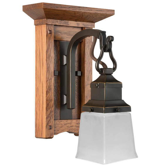  A short, wall mounted sconce lantern made with quarter sawn oak like Stickley furniture. The fixture is mounted on a metal hook with an oil rubbed bronze finish and a rectangular, white glass shade.