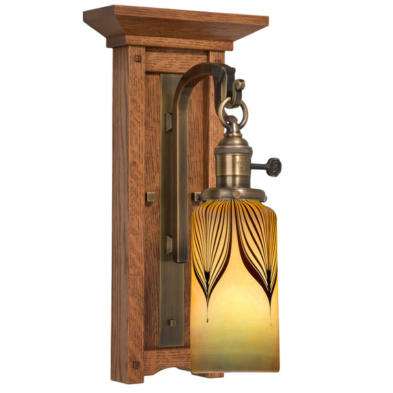  A tall, wall mounted sconce lantern made with quarter sawn oak like Stickley furniture. The fixture is mounted on a metal hook with an aged brass finish, turn key socket and a cylindrical, blown glass shade.