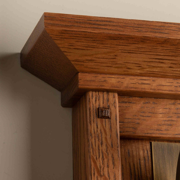  Corner wall plate detail of a tall, wall mounted sconce lantern made with quarter sawn oak like Stickley furniture. The fixture is mounted on a metal hook with an aged brass finish, turn key socket and a curvy, blown glass cherry blossom shade.