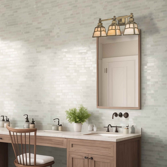  A reproduction turn-of-the-century Arts & Crafts bathroom vanity light fixture with three lanterns that have an aged brass finish and metal-framed glass shades with an arch design. The fixture is installed above a mirror in a tiled bathroom with a lot of amenities including a dressing chair.