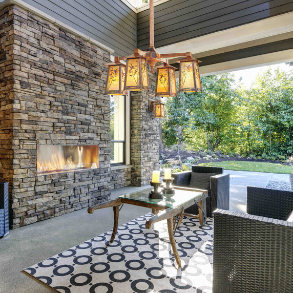  A rustic copper chandelier hangs above the seating area of a a back patio with a stone fireplace and linear, wicker furniture.