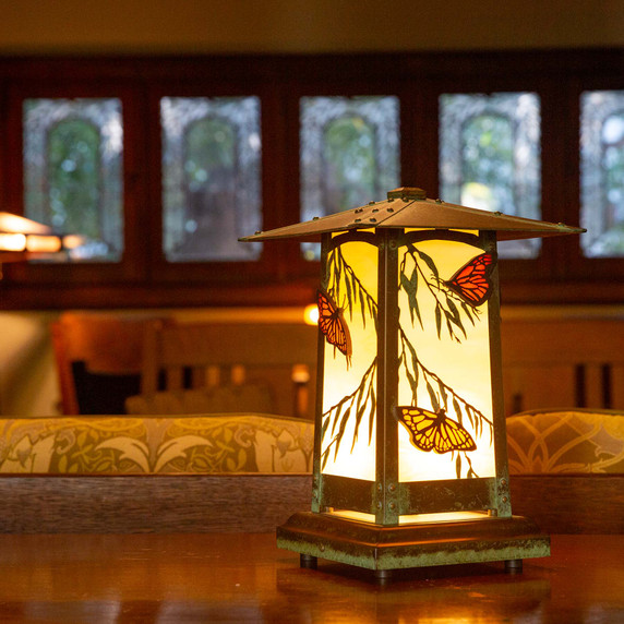  A rustic style portable table lamp with butterfly accents sits illuminated in the living room of a historic home.