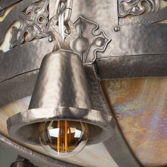  Close-up of chain-hung bell shade with Edison bulb illumination and ornate pewter scrollwork background featuring iridescent glass panels.