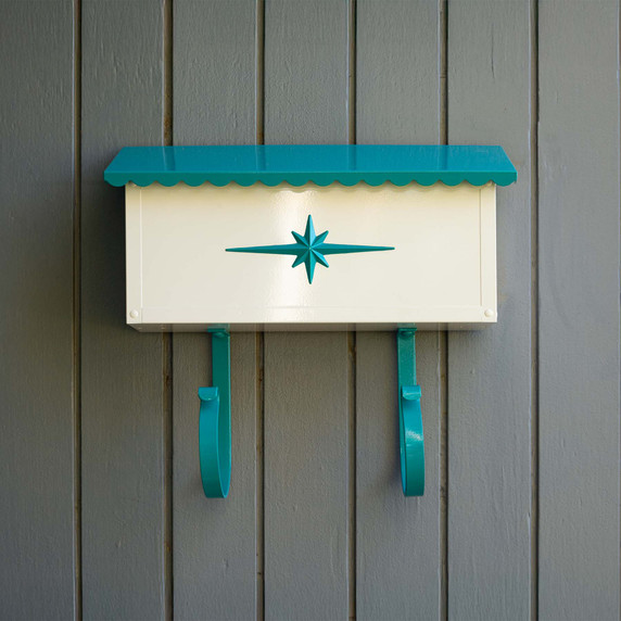  A glossy Americana style mailbox with teal accents, starburst medallion and magazine rack against a gray wall.