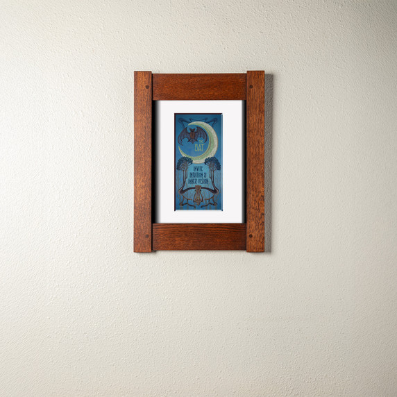 An archival print of a bat and crescent moon in a mortise and tenon oak frame and soft white mat.