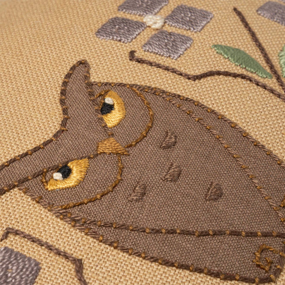  Closeup photo of a dark linen beige throw pillow featuring a embroidered design of petite owl artwork and tree branches.