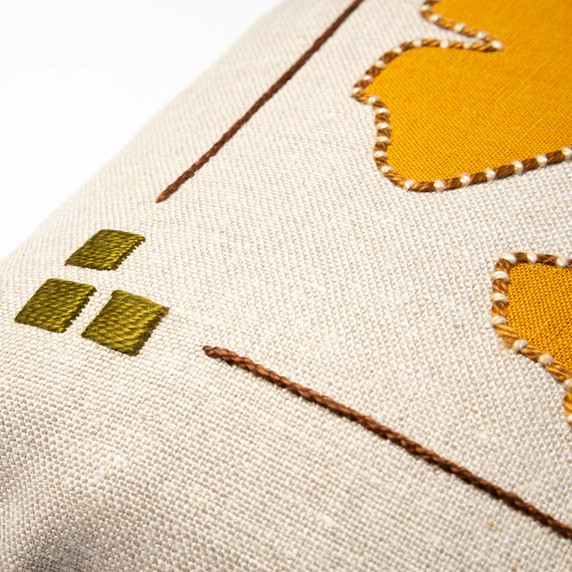  Closeup photo of a linen beige throw pillow featuring a Craftsman style frame embroidered artwork of three squares and rust embroidered border.