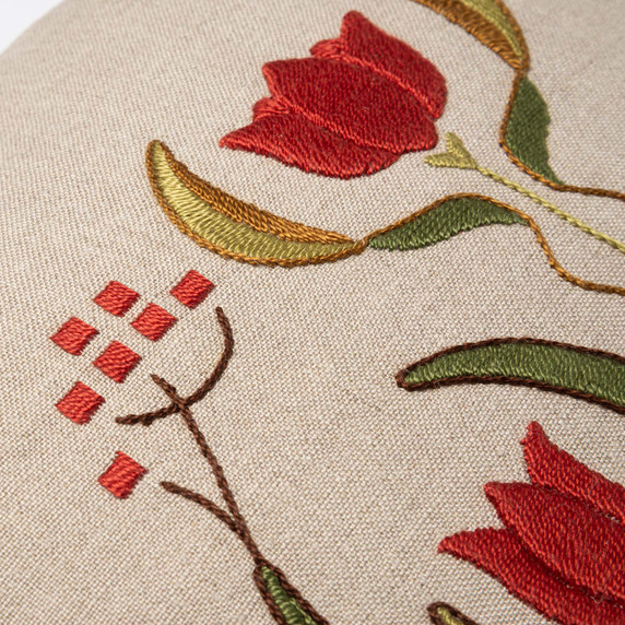  Closeup photo of a linen beige throw pillow featuring embroidered artwork of a red tulips and red squares.