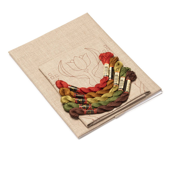  DIY embroidery kit for a tulip pillow design, showing folded natural linen stamped with a tulip alongside arranged embroidery thread skeins in a variety of colors.