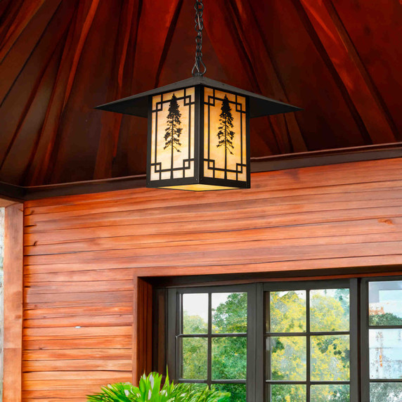  A linear Arts & Crafts chain mounted pendant light fixture with a black finish, warm colored glass and the silhouette of a giant Sequoia tree. The lantern is hanging from the ceiling of a home exterior near a window.