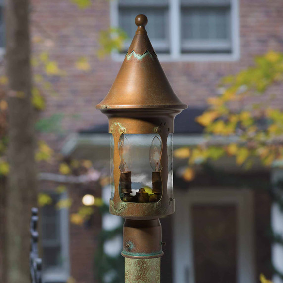  A Victorian or storybook style lantern mounted on a brass post in front of a brick building.