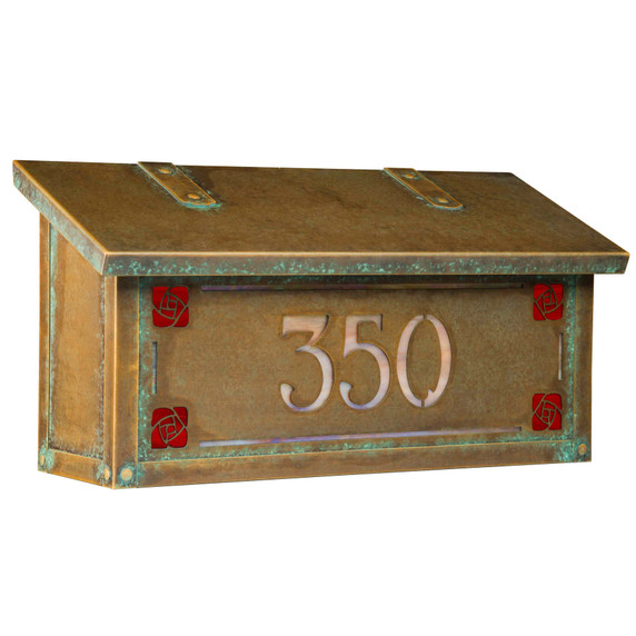  Three-quarter view of a Craftsman style mailbox featuring the Hunter Rose (sometimes called the Mackintosh Rose) as corner design accents. The mailbox has an aged patina finish and house address numbers backed by iridescent glass.