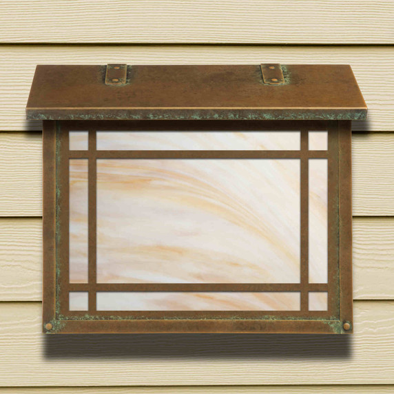  A large, Mission style mailbox with a linear border pattern, aged patina finish and warm white glass on neutral toned siding.