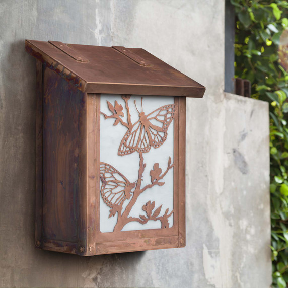  A small vertical mailbox against a concrete wall. It's made from copper and white art glass and features butterfly artwork.