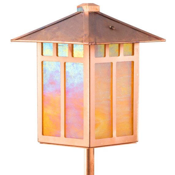  Close up of an artistic garden lantern on a post with a raw copper finish, linear Craftsman design and iridescent glass. The light fixture is not illuminated.