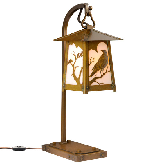  A beefy, rustic table lamp on a hooked arm with Gothic literature raven silhouettes in trees, an aged brass finish and off white glass.