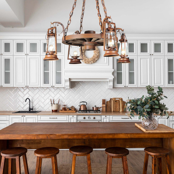  A rustic wooden wagon wheel chandelier with hanging bronze lantern lights, suspended over a rustic wooden kitchen island in a bright, modern farmhouse kitchen.