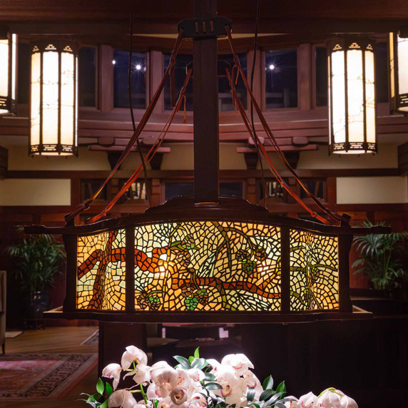  An intricate wood and stained glass chandelier over a bouquet of white flowers in a large space featuring other chandeliers. 