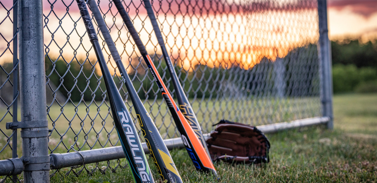 Baseball bats leaning against a chain link fence with a sun set in the background