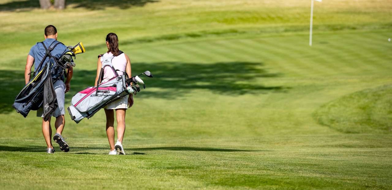 two golfers walking across the course carrying their clubs