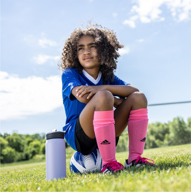 Young Girl in a soccer uniform sitting on a soccer ball on a green soccer field