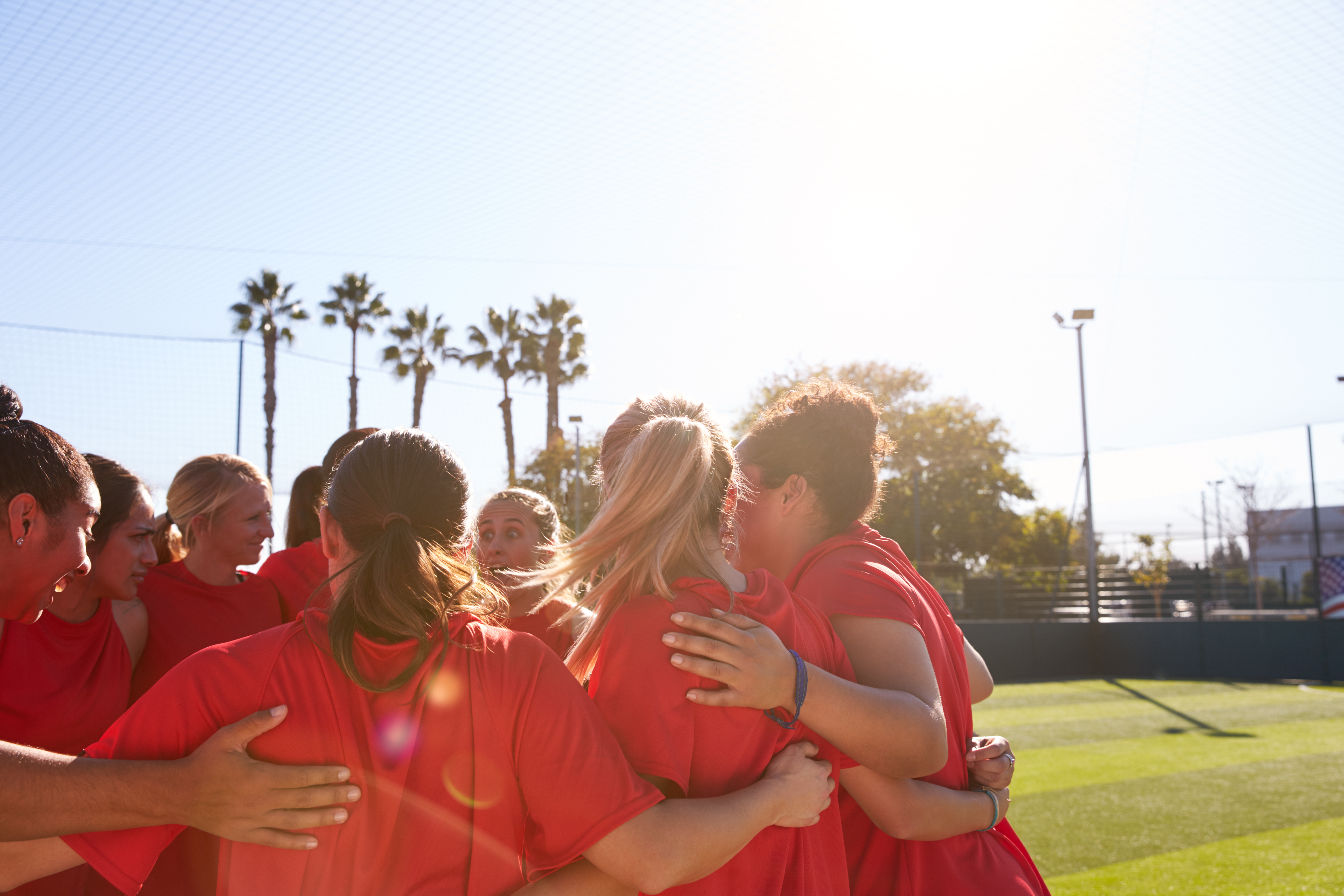 Women’s sports team in red shirts huddled together on an outdoor field