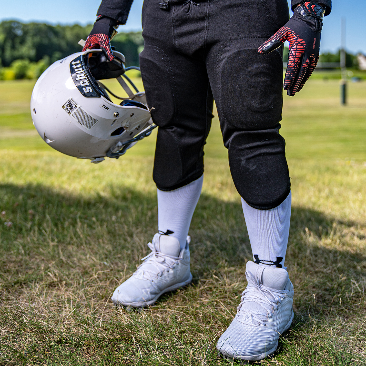 football player holding a helmet. picture is from the knees down