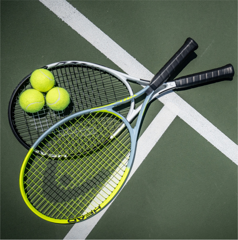 two tennis rackets laying on a tennis court with three tennis balls on top