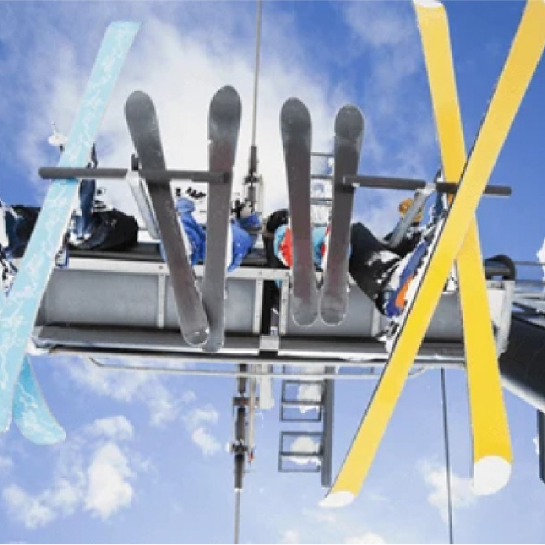 View from beneath a full seat on a ski lift showing 2 children and 2 adult skiers with a blue sky in the background 