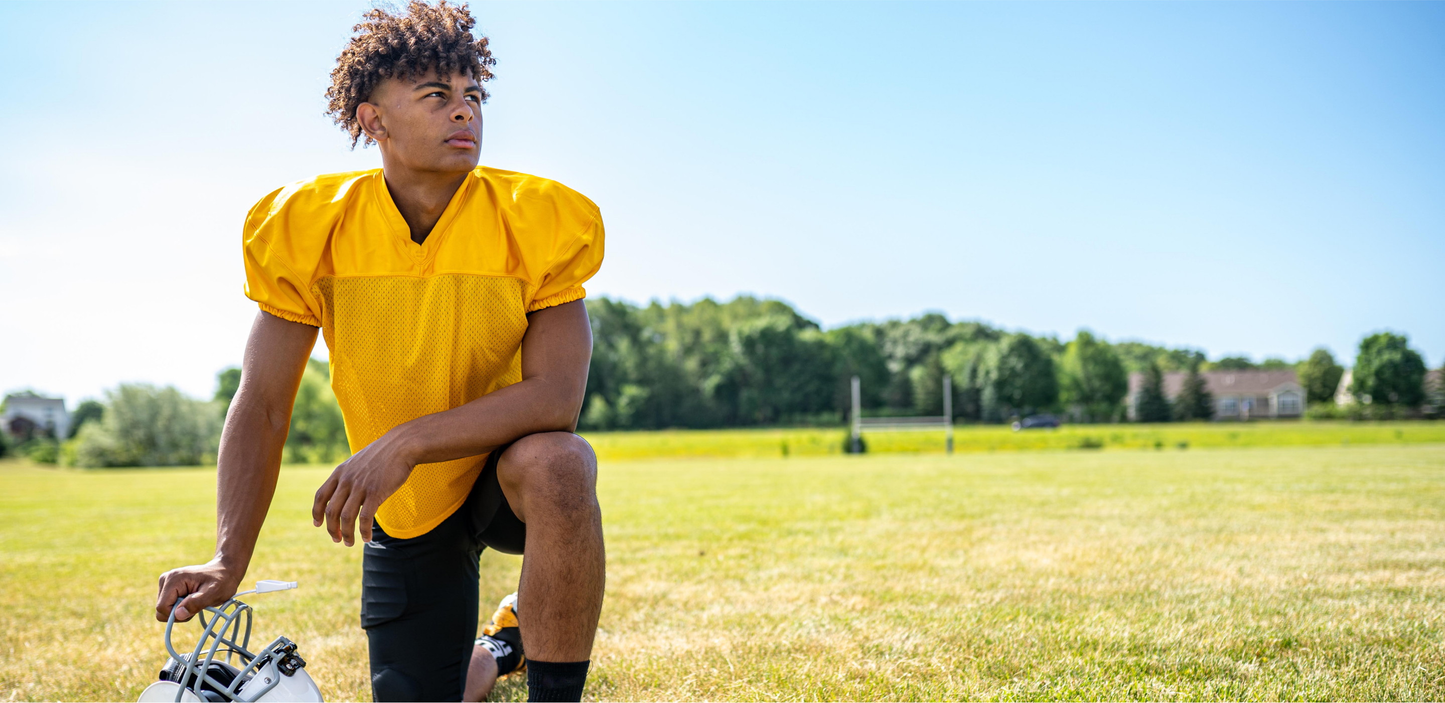 young football player kneeling on the field looking into the sky with a determined look