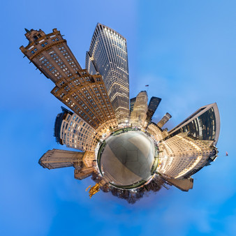 A 360-degree panoramic photograph of Grand Army Plaza in New York City during the blue hour, featuring illuminated buildings surrounding a distorted reflection of the plaza, creating a spherical effect.