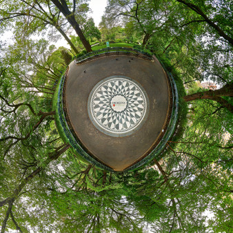 A 360-degree panoramic Spherescape of the Imagine Mosaic in Strawberry Fields, Central Park, surrounded by lush green trees in the soft light of early morning.