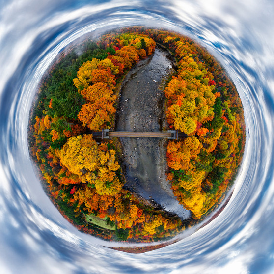 A black and white 360-degree panoramic photograph of the Wire Bridge spanning the Carrabassett River in New Portland, Maine, framed by a sphere of surrounding trees in lush foliage