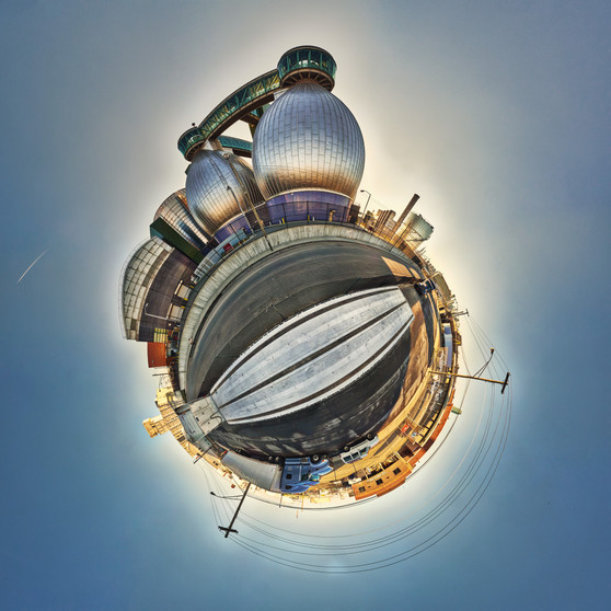 A late afternoon 360-degree panoramic spherescape of the digesters at the Newtown Creek Wastewater Treatment Plant in Greenpoint, Brooklyn, with industrial structures illuminated by the setting sun.
