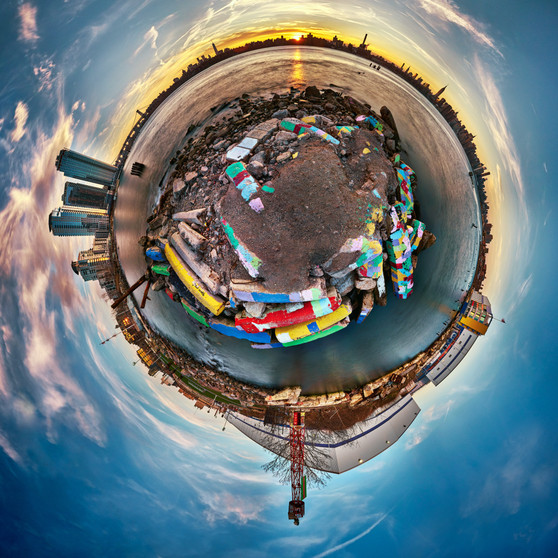 A 360-degree panoramic Spherescape taken from the edge of the East River in Greenpoint, capturing the colorful pier remains and the sweeping Manhattan skyline at sunset.