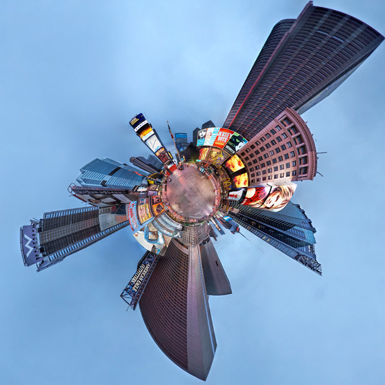 A 360-degree panoramic image of Times Square during the blue hour of pre-dawn, showcasing illuminated billboards and skyscrapers under a tranquil blue sky in a spherical composition.