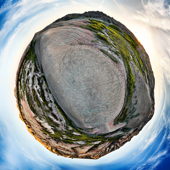 360-degree panoramic view of Badlands National Park at sunset, with colorful striations and greenery, presented in a spherical form.