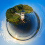 Aerial 360 panoramic image of Doubling Light in Arrowsic, Maine, showcasing the lighthouse amidst vivid greenery, bordered by the gentle blue waters, under a wide, expressive sky