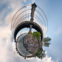 A 360-degree panoramic Spherescape of the Manhattan Bridge in NYC, with the bridge’s cables and structure dramatically arched over the surrounding city and waters, framed by a cloudy sky.