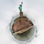 A 360-degree panoramic color image of the Statue of Liberty on an overcast afternoon, with a muted color palette of grays and greens, encircled by small figures against a continuous sky and water horizon