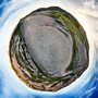 360-degree panoramic view of Badlands National Park at sunset, with colorful striations and greenery, presented in a spherical form.