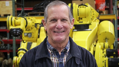 Smiling TIE Industrial technician standing in front of large yellow Fanuc robot