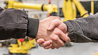 Two hands shaking in front of Fanuc robots