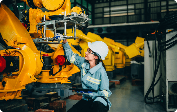 Technician servicing yellow Fanuc robot arm with replacement parts in the factory